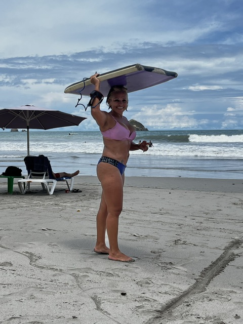 Guest holding a bodyboard overhead at the shore