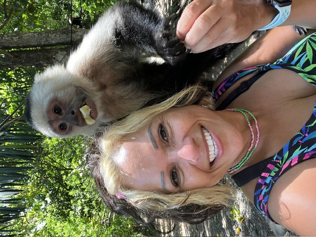 Scheyla smiling with a capuchin monkey eating fruit on her shoulder
